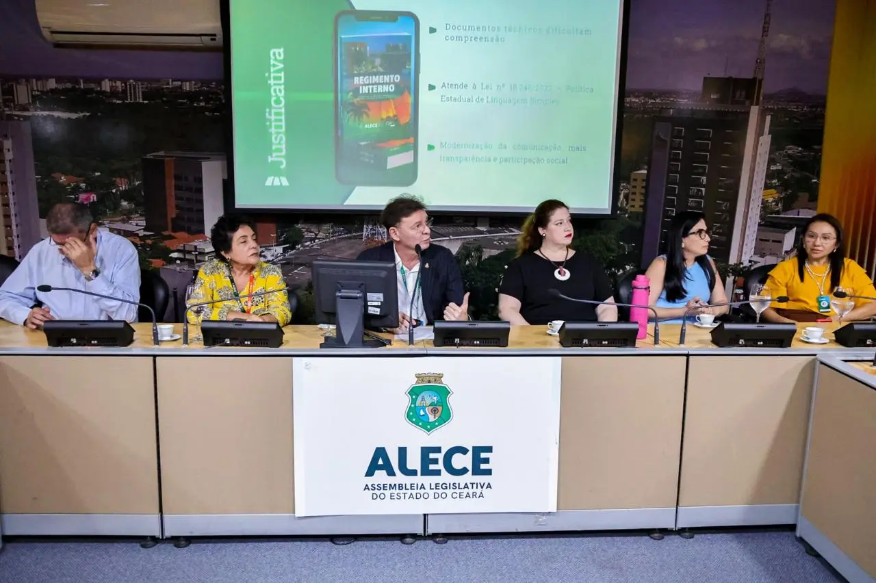Mesa de painel com cinco participantes, incluindo três mulheres e dois homens, apresentando em um evento. No telão, aparece um slide sobre Regimento Interno e o logotipo da ALECE no púlpito.