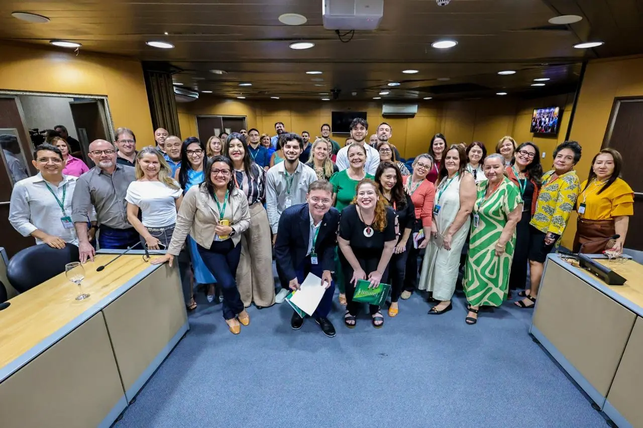 Grupo de aproximadamente 30 participantes, incluindo homens e mulheres, em uma sala da Assembleia Legislativa, posando para uma foto.