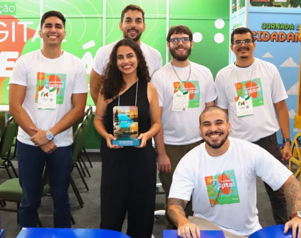 Seis participantes em estande com painéis ‘Transformação Digital no Ceará’ e ‘Jornada da Cidadania’; uma mulher ao centro segura um troféu.